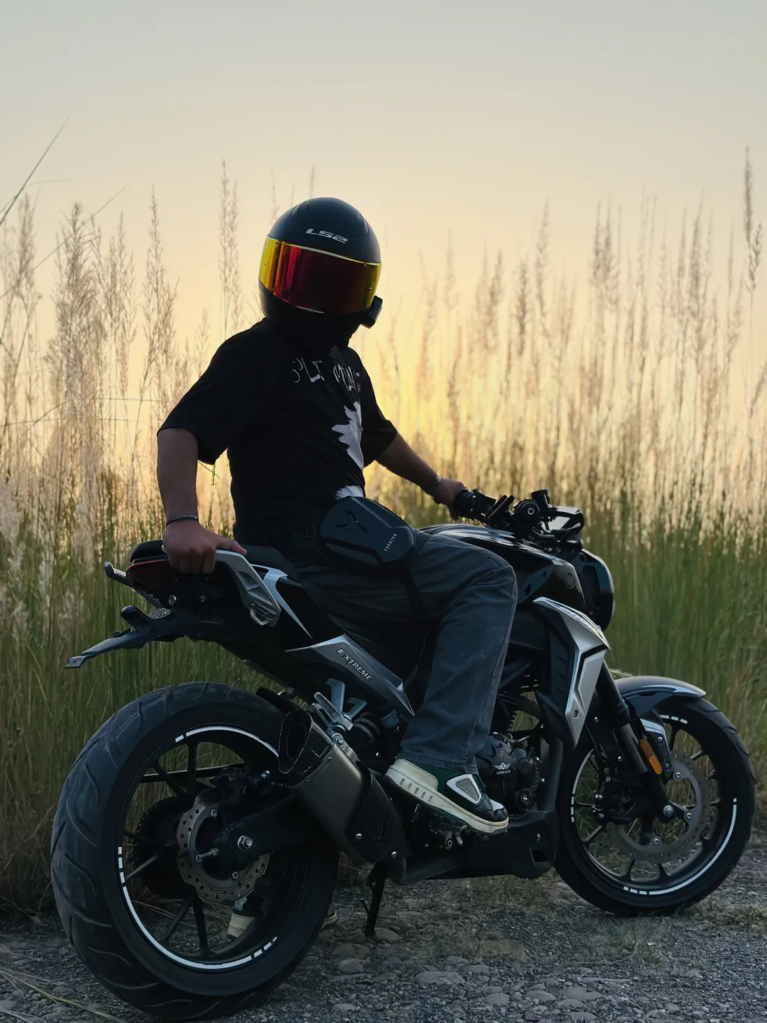 Raheel on his black naked bike in tall grass at sunset